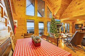 A wooden cabin interior with a dining area, a Christmas tree, and a kitchen.