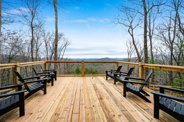 A wooden deck with black Adirondack chairs and a wooden railing.