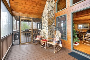 A wooden deck with rocking chairs, a stone wall, and a Christmas tree.