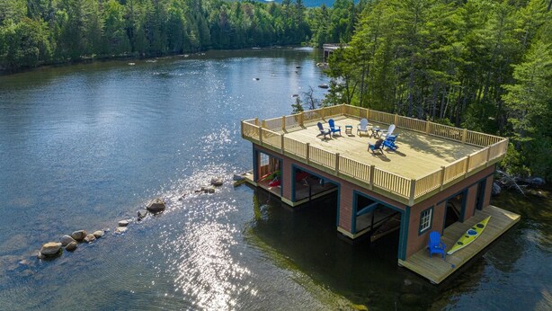 A wooden dock with a deck, surrounded by a forest and a lake. - Camp Balsam | Lake Placid Lakefront Estate with Indoor Pool & Boathouse (Lake Placid)