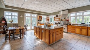 A spacious kitchen with a large island, wooden cabinets, and ample natural light from large windows. - Camp Balsam | Lake Placid Lakefront Estate with Indoor Pool & Boathouse (Lake Placid)