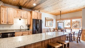 Una cocina con armarios de madera, encimera de granito, refrigerador negro y una zona de bar con taburetes.