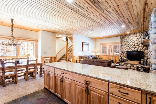 A spacious living area with a stone fireplace, wooden ceiling, and a large TV. - New! Exquisite Log Cabin home-HOT TUB, FIREPLACE, AC, Garage, walk to SKI lift (Park City)