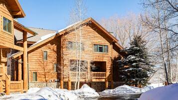 A log cabin with a stone foundation, a wooden porch, and a snow-covered landscape.