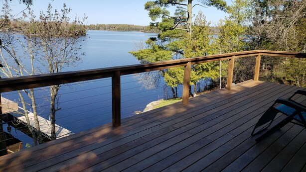 A wooden deck with a railing overlooking a lake, surrounded by trees. - Northern Paradise on Lake Vermilion - Year Round Home (Tower)