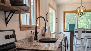 A kitchen with a black stove, a sink, and a window. There is a rug on the floor and a chair in the background. - Northern Paradise on Lake Vermilion - Year Round Home (Tower)