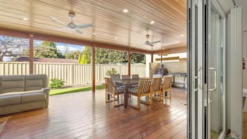 A covered outdoor patio with a dining table and chairs, a sofa, and ceiling fans.