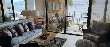A spacious living room with a large sliding glass door leading to a balcony with a view of the ocean.