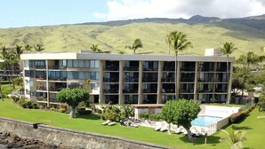 Un hotel de varios pisos con balcones, piscina y vistas a colinas y aerogeneradores al fondo.