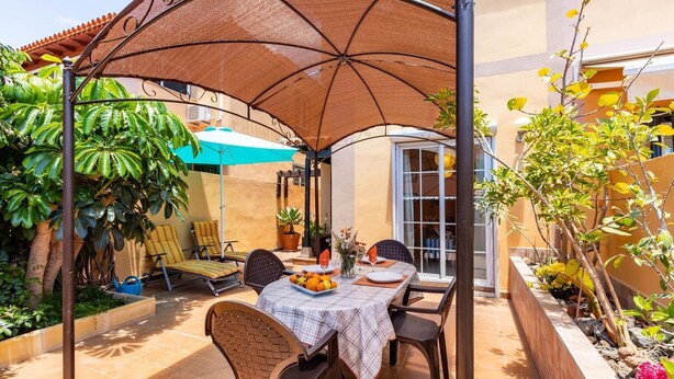 En patio med borde og stole til to personer, under en stor parasol.