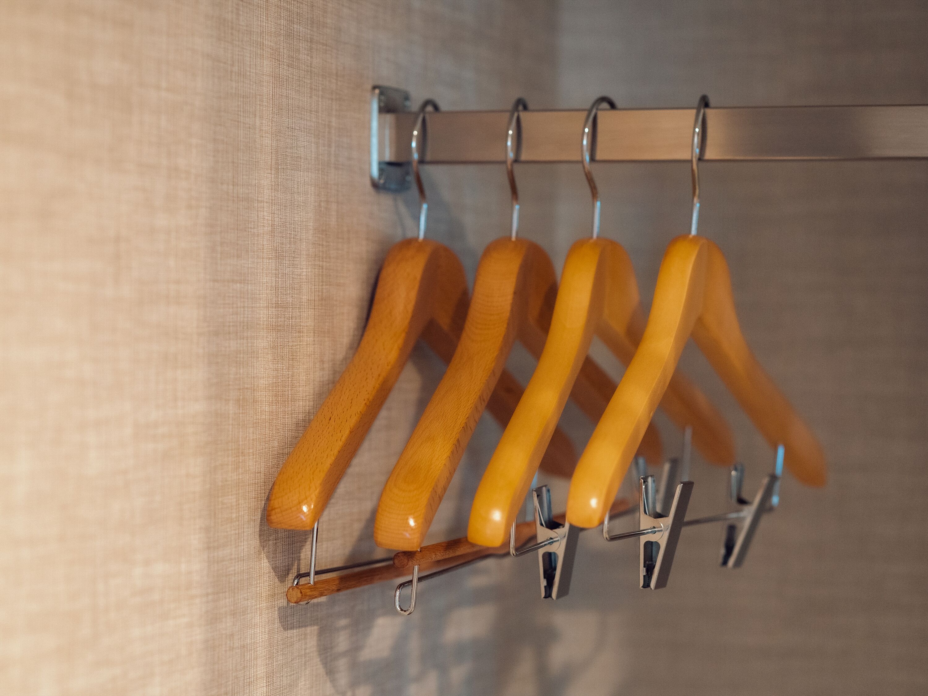 A wooden hanger rack with five hangers against a textured wall.