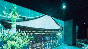 Een modern interieur met een groot digitaal scherm waarop een traditioneel gebouw staat afgebeeld, potplanten en een betegelde vloer.