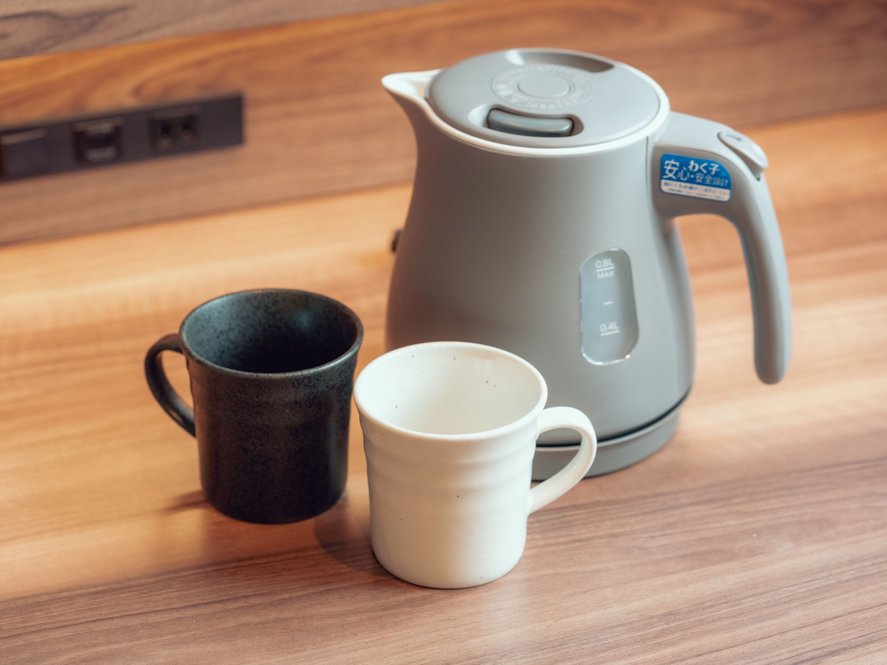 A kettle and two cups on a wooden surface.