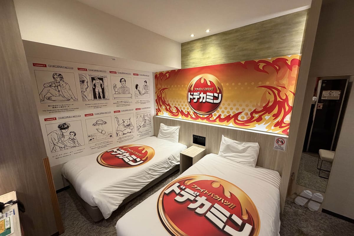 Une chambre d’hôtel avec deux lits, une grande affiche murale et une porte avec une pancarte.