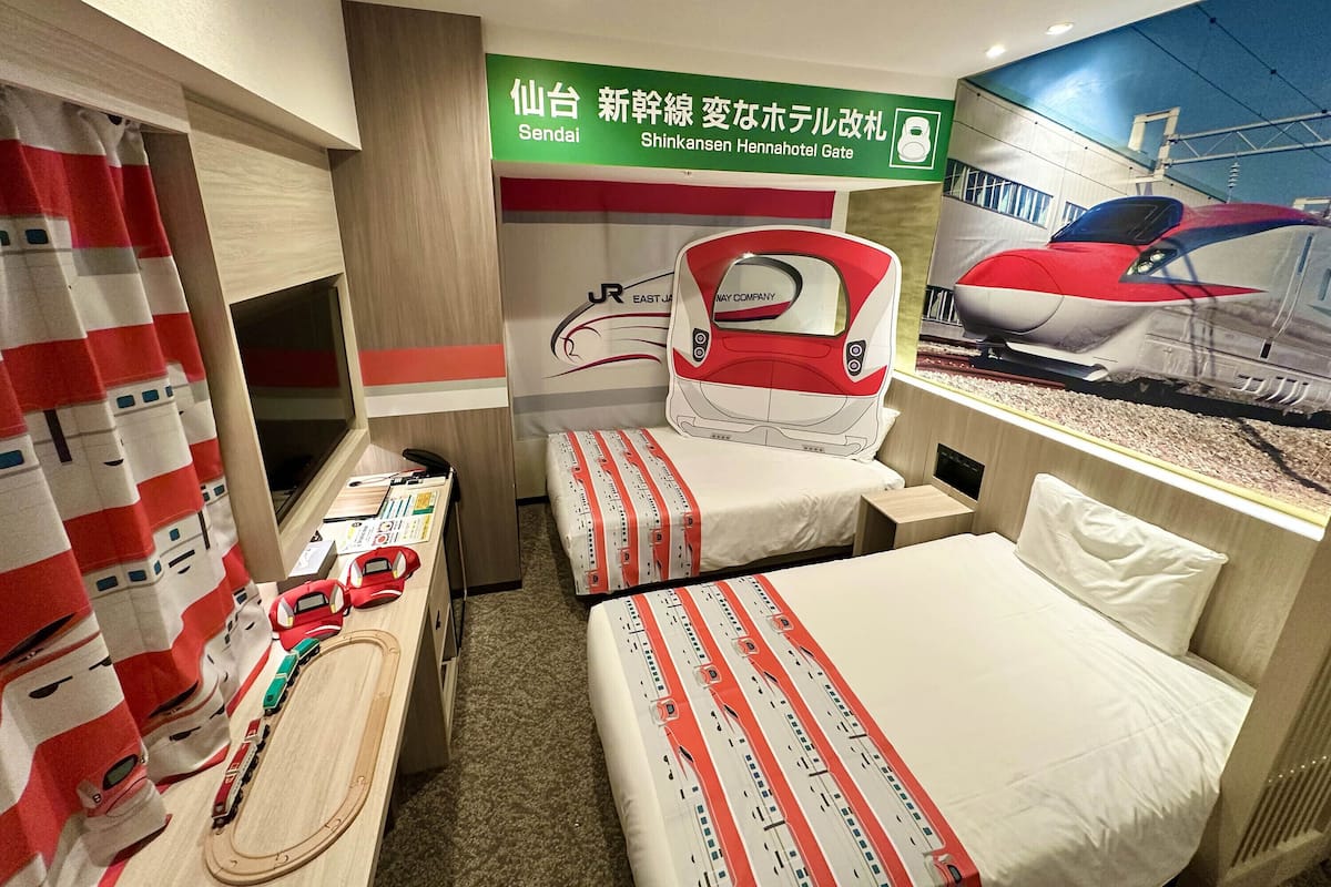 Une chambre d’hôtel avec deux lits, un bureau, une petite table sur laquelle est posé un train jouet, et une fresque représentant un train.
