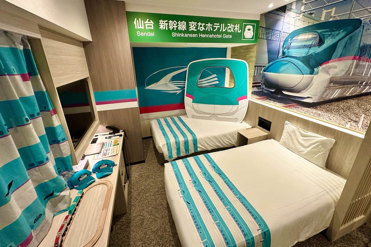 Une chambre d’hôtel avec un lit, un bureau, une chaise et une grande fenêtre donnant sur les voies ferrées.