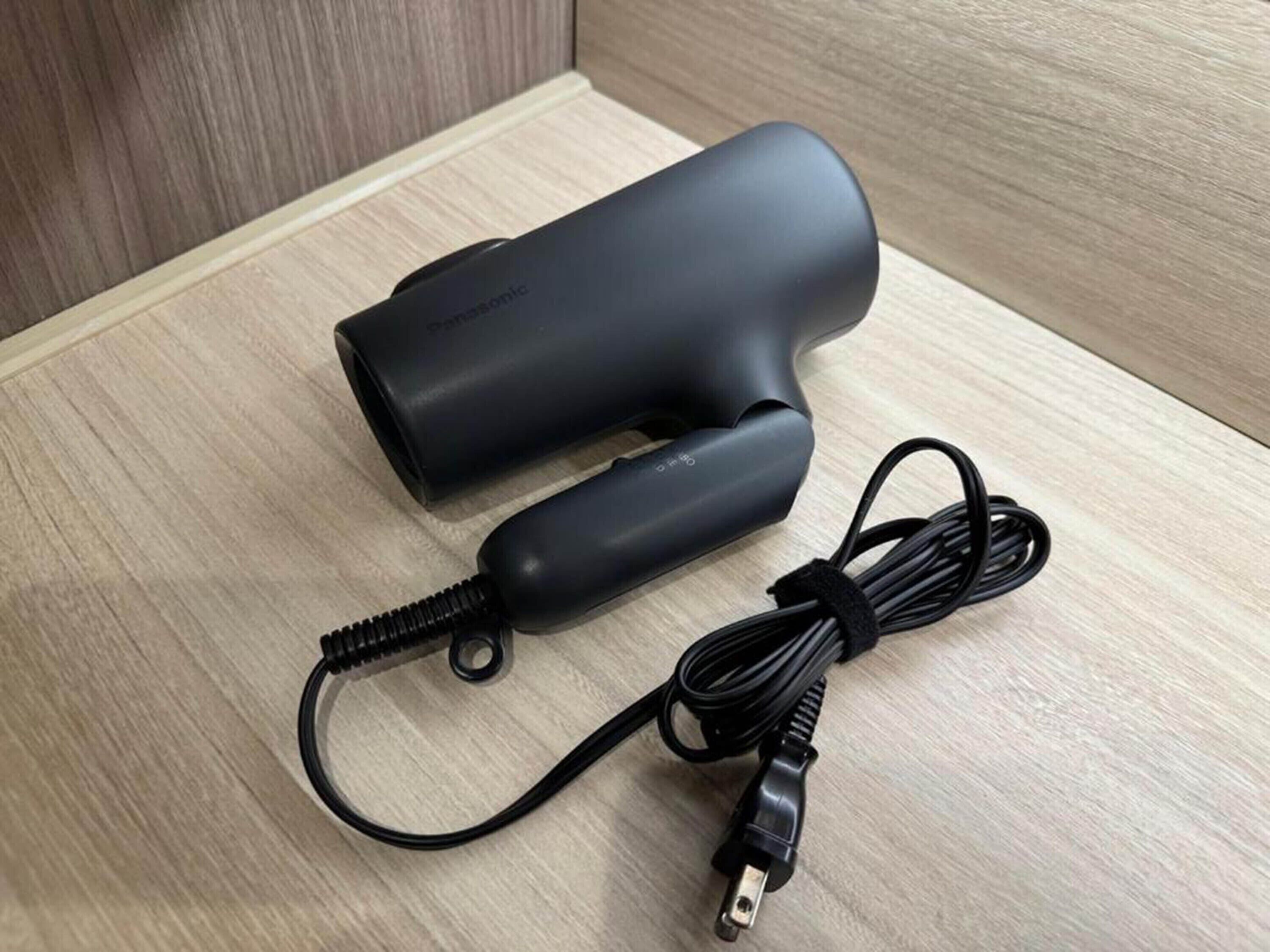 Un cargador portátil negro con cable y conector USB sobre una superficie de madera.