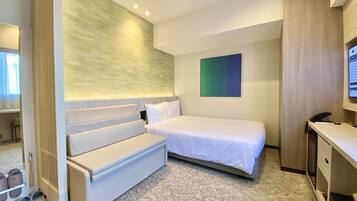 A hotel room with a bed, a seating area, a desk, and a television.