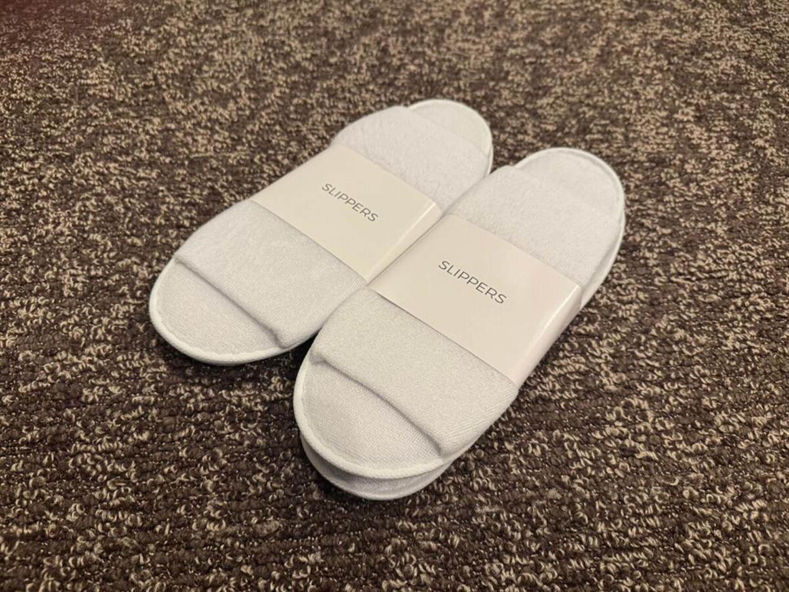 A pair of white slippers with 'SLIPPERS' text on a textured carpet.