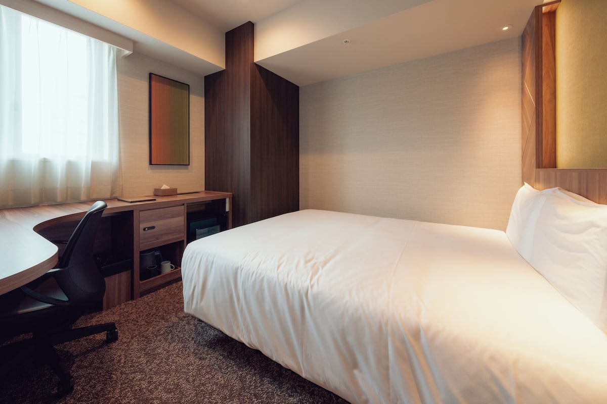 Une chambre d’hôtel équipée d’un lit, d’un bureau, d’une chaise et d’une grande fenêtre avec des rideaux.