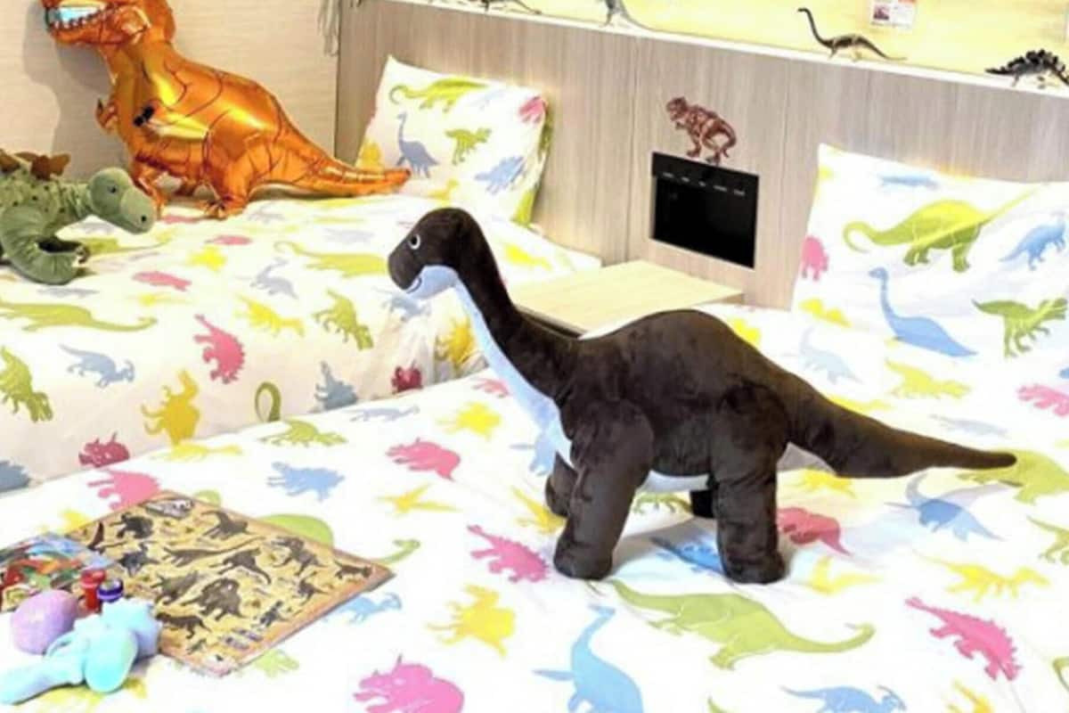 Un lit avec une literie sur le thème des dinosaures, un jouet dinosaure et un livre sur les dinosaures.