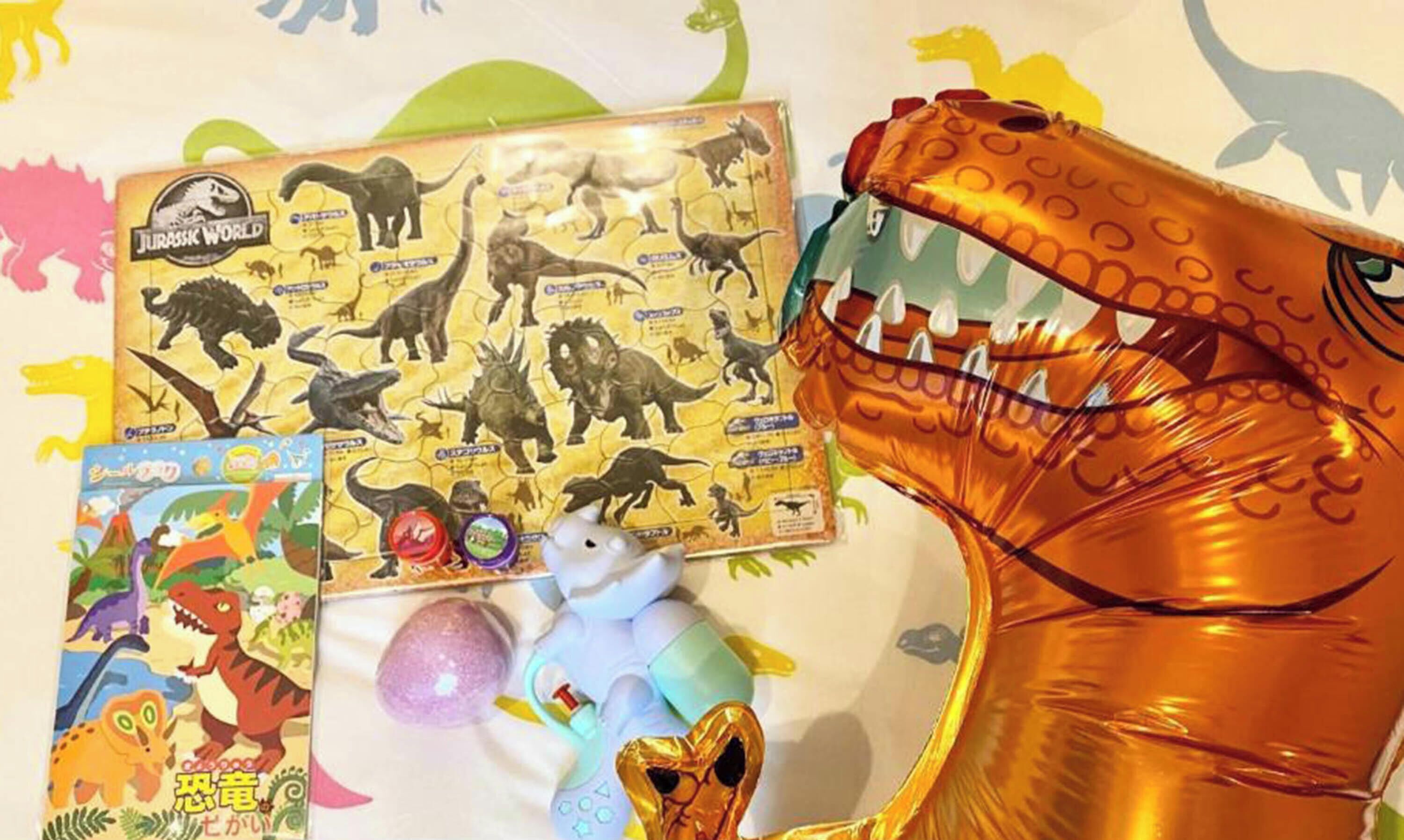 Uma caixa de lembrancinha com tema de dinossauro, um brinquedo de pelúcia e um dinossauro inflável grande.