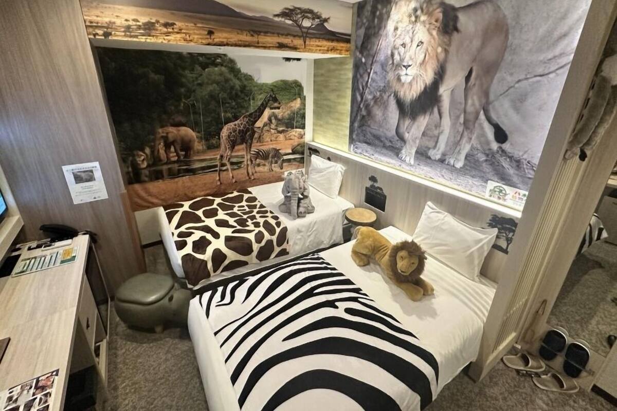 Une chambre avec un lit orné d’un motif zébré, un coussin à motif girafe, un coussin à motif lion et un animal en peluche.