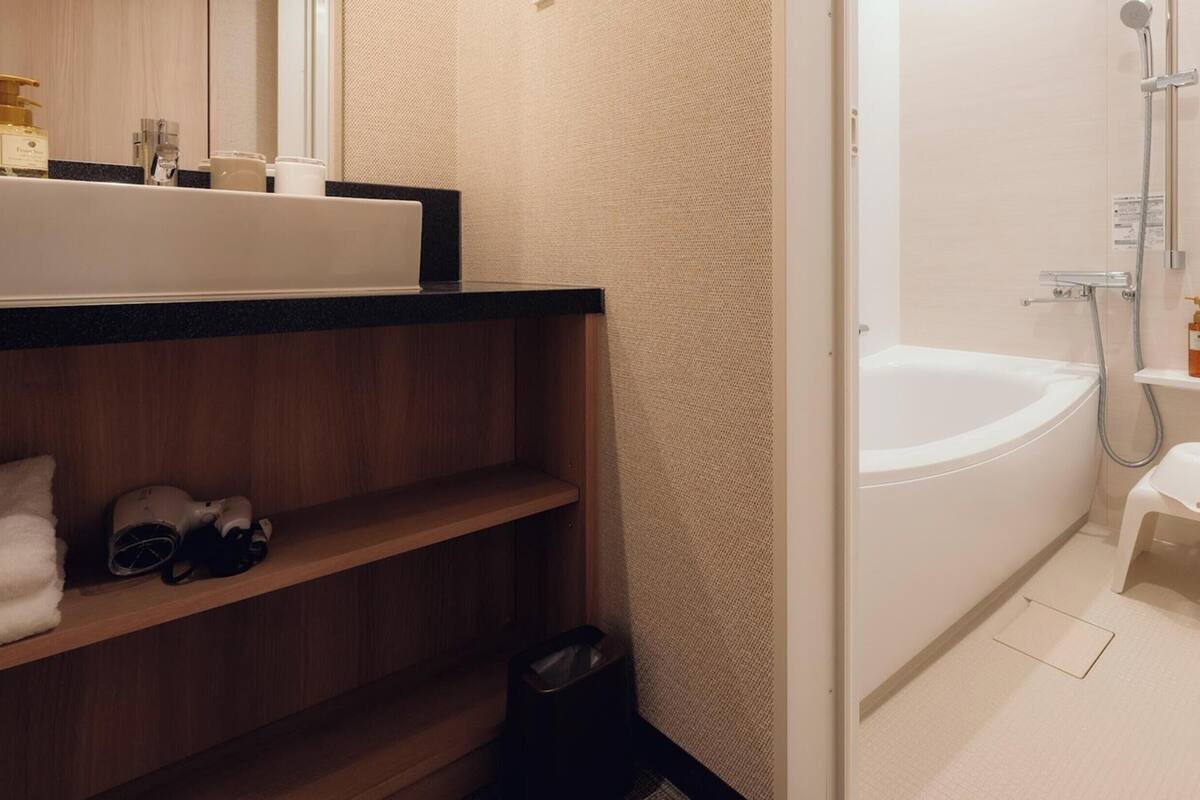 Une salle de bain avec une baignoire, une douche, un petit tabouret et une étagère contenant des articles de toilette.