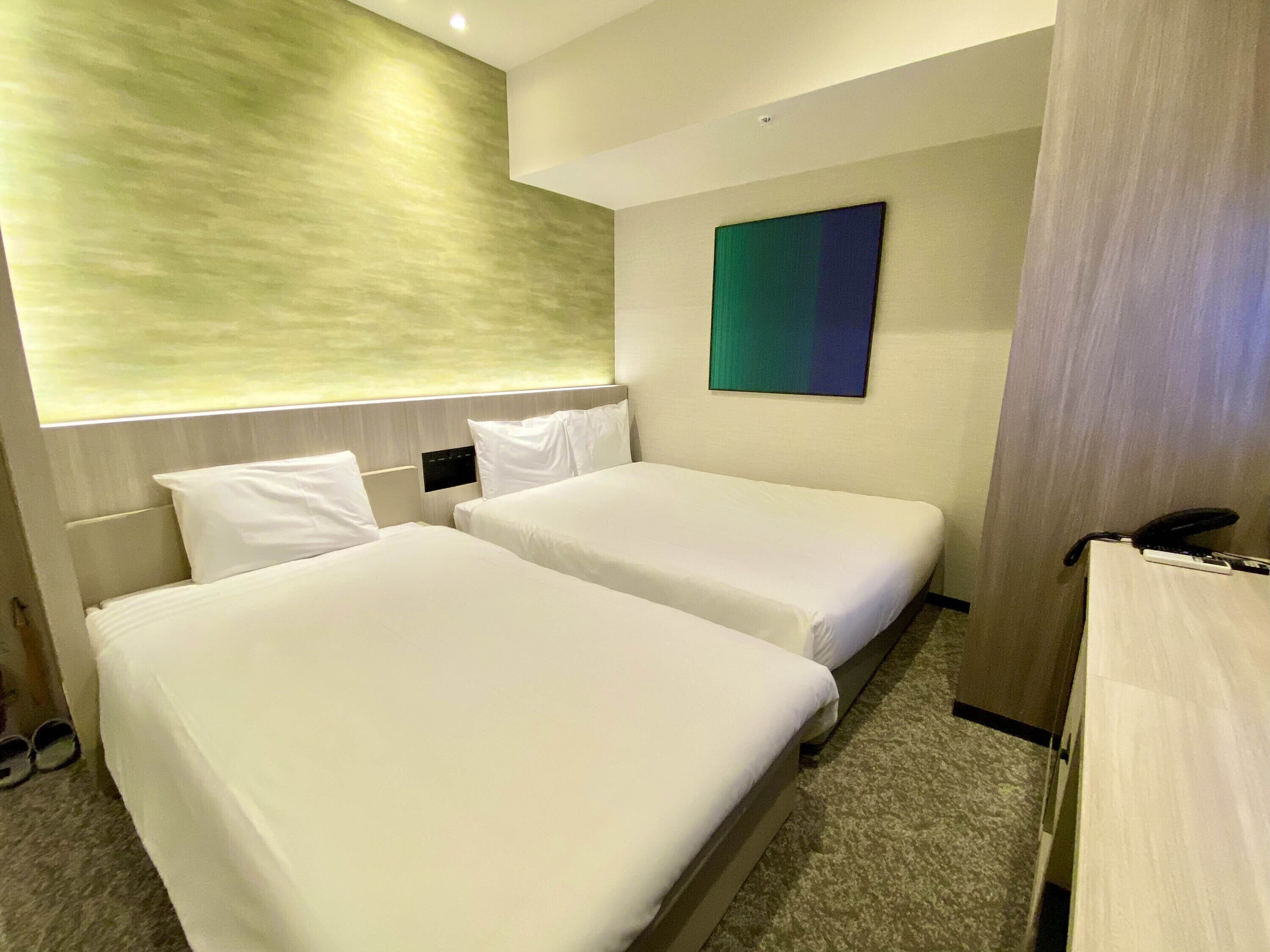Ein Hotelzimmer mit zwei Betten, einem Kopfteil, einem an der Wand montierten Telefon und einem Gemälde.