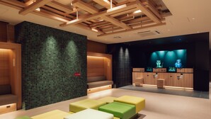 Een moderne lobby met houten balken in het plafond, een wand betegeld met groen en een zithoek met kleurrijke kussens.