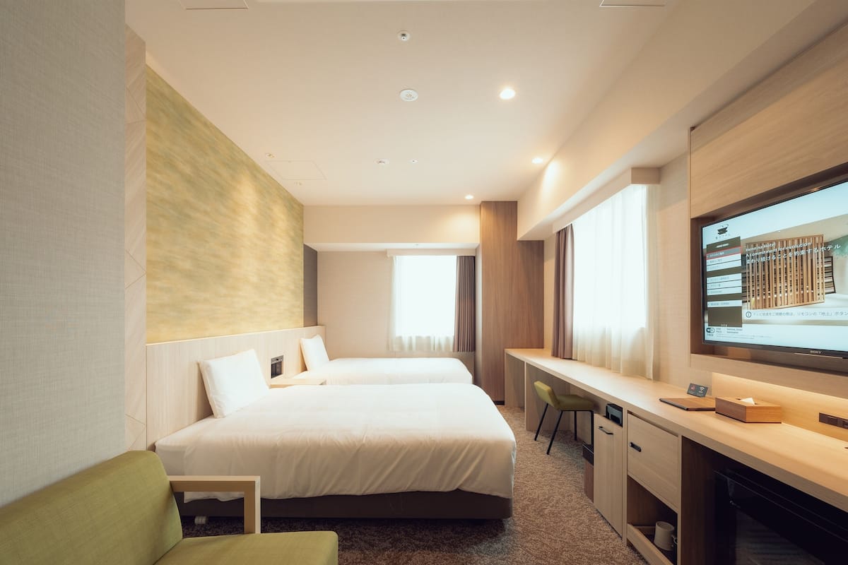 Une chambre d’hôtel avec deux lits, un bureau, une télévision et un fauteuil vert.