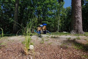 A playground with a slide and climbing structures surrounded by trees.