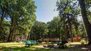 Un parc avec des bancs verts, une balançoire et un petit bâtiment.