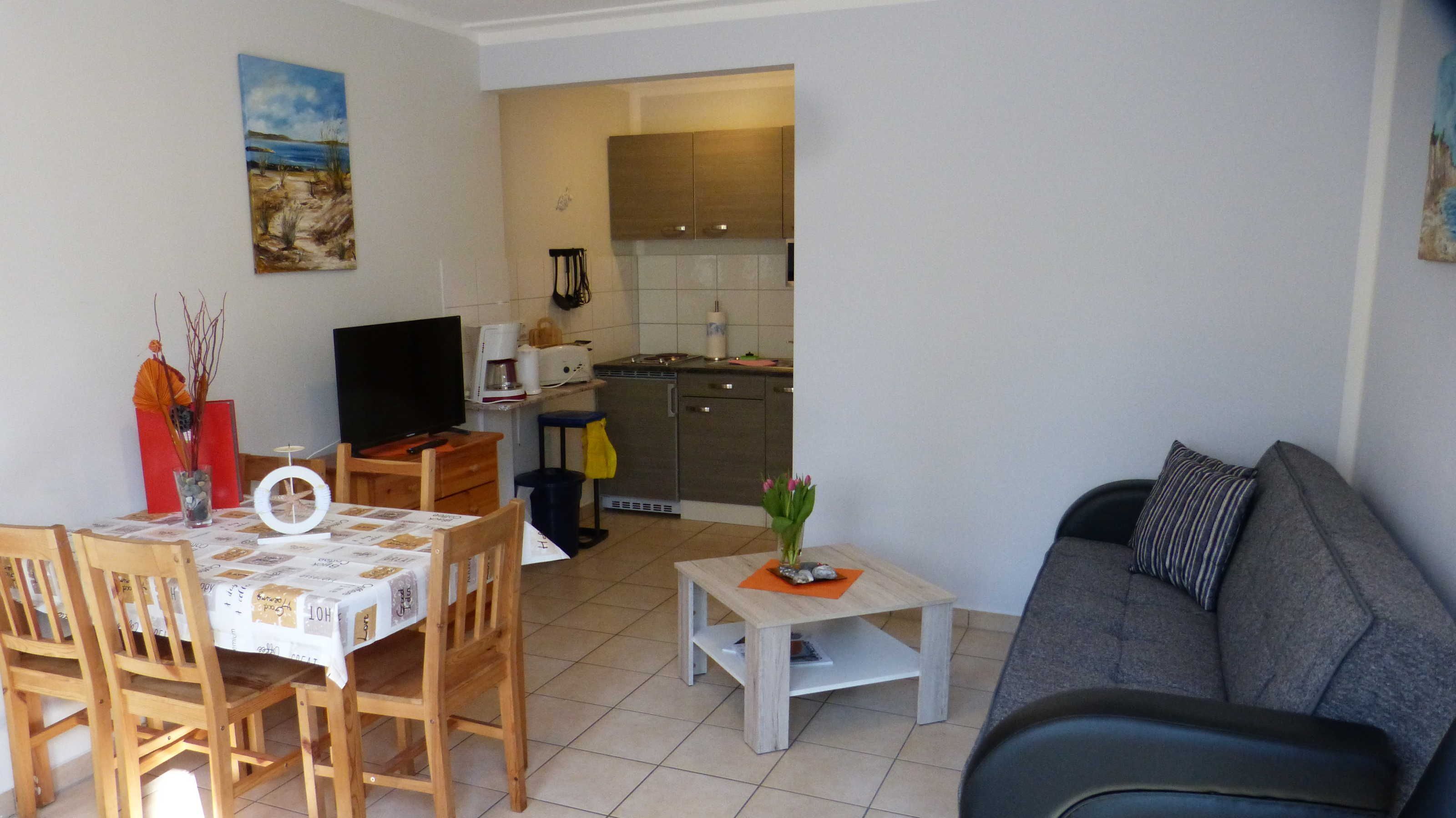 A compact living space with a dining area, a sofa, a TV, and a kitchen in the background.