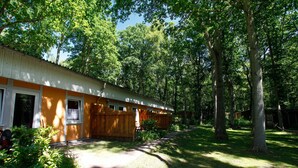 Un bâtiment d’un seul étage, avec une façade en bois, entouré d’une zone boisée.