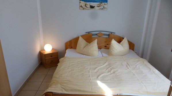 A bedroom with a wooden headboard, a bedside table with a lamp, and a bed with pillows.