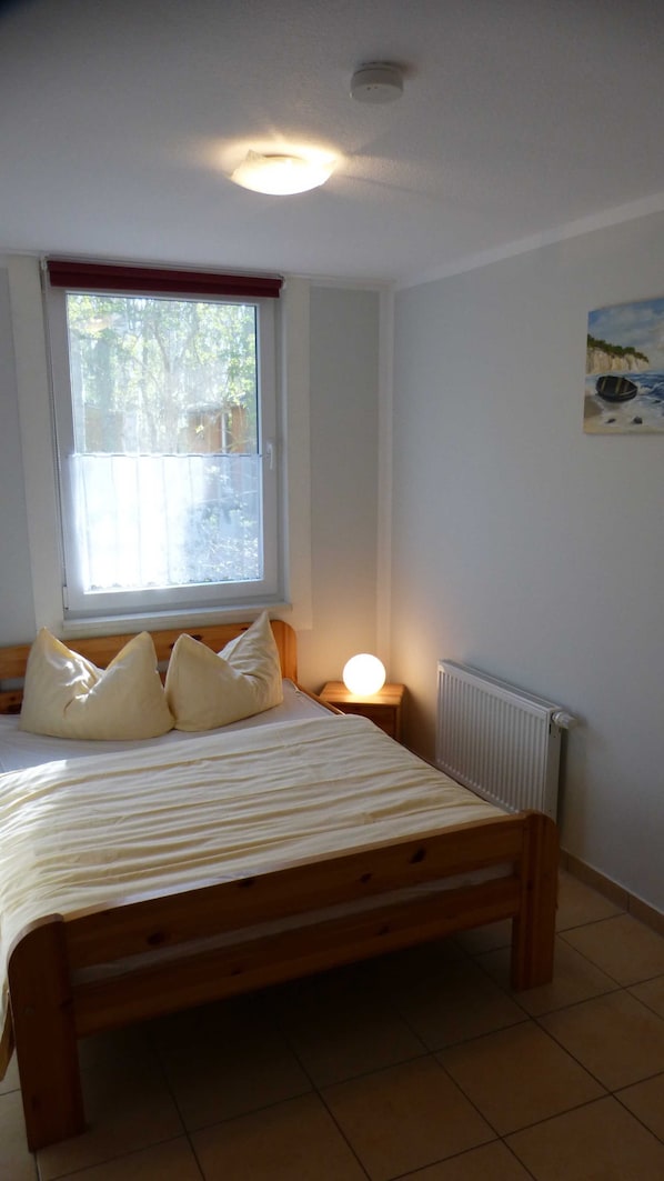 A bedroom with a wooden bed, a window with a view of trees, a nightstand with a lamp, and a radiator.