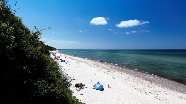 A beach with tents and people, clear skies, and calm water.