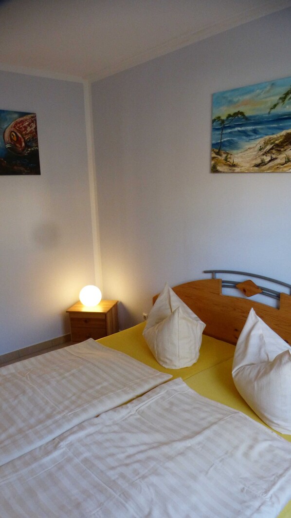 A bedroom with a bed, pillows, a nightstand with a lamp, and two wall paintings.