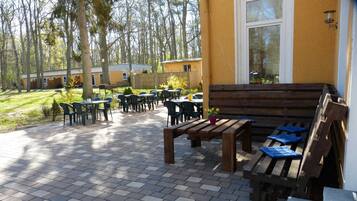 Eine Gartenpatio mit Holzbänken und Tischen, umgeben von einem Garten und Bäumen.