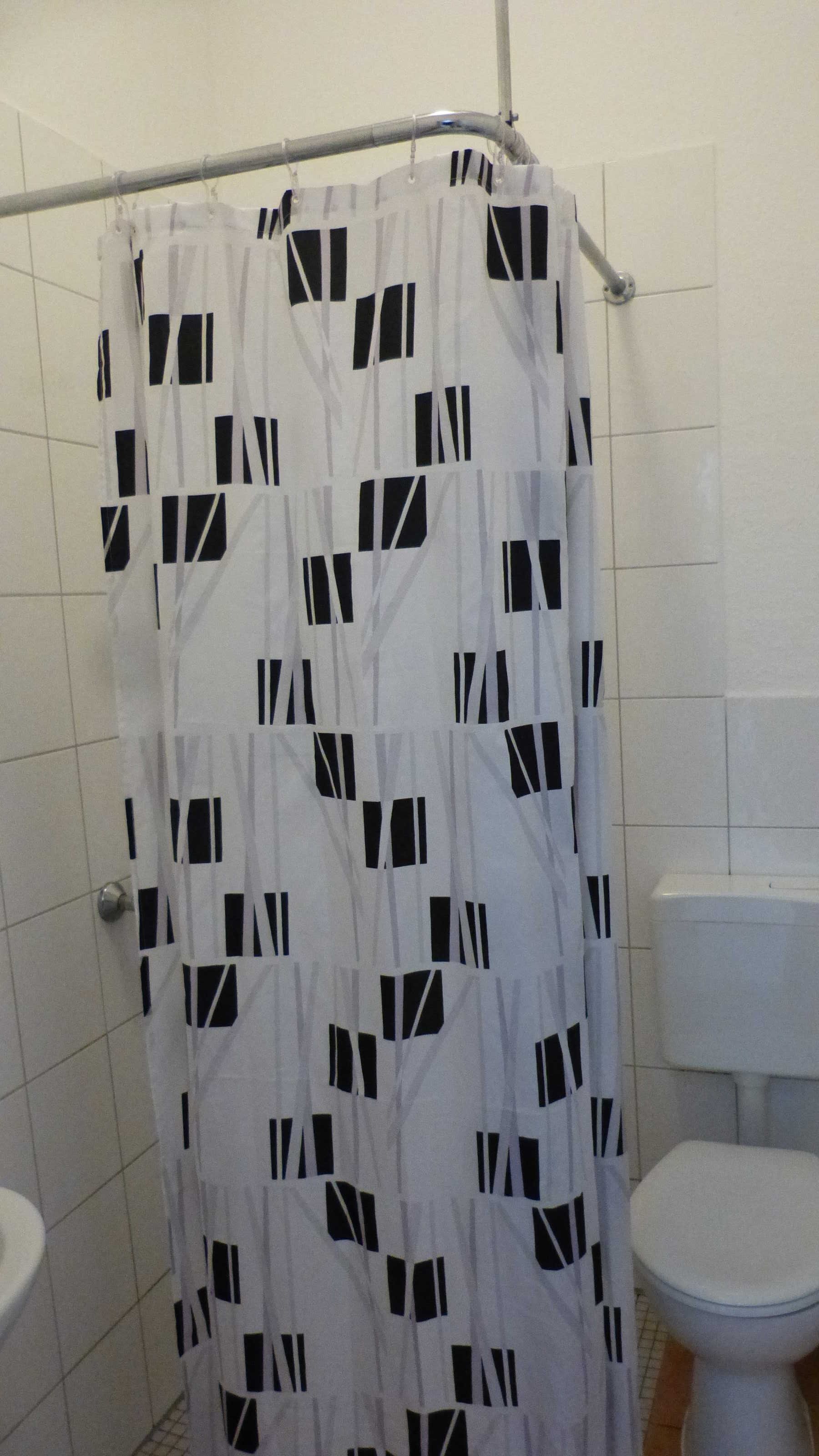 Un baño con cortina de ducha estampada con un motivo geométrico, un inodoro y una pared de azulejos.