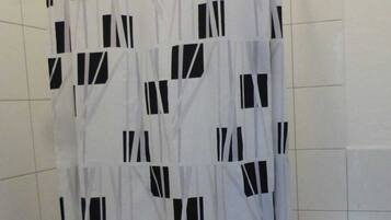 Un baño con cortina de ducha estampada con un motivo geométrico, un inodoro y una pared de azulejos.