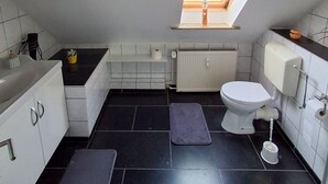 A compact bathroom with a skylight, a toilet, a radiator, and a small sink.