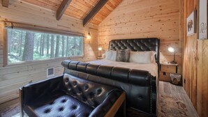 Ein gemütliches Schlafzimmer in einer Hütte mit einem großen Bett, einer Lederbank und einem Fenster mit Blick auf einen Wald.