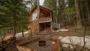 Eine Hütte mit Balkon, umgeben von Bäumen und einer Feuerstelle.