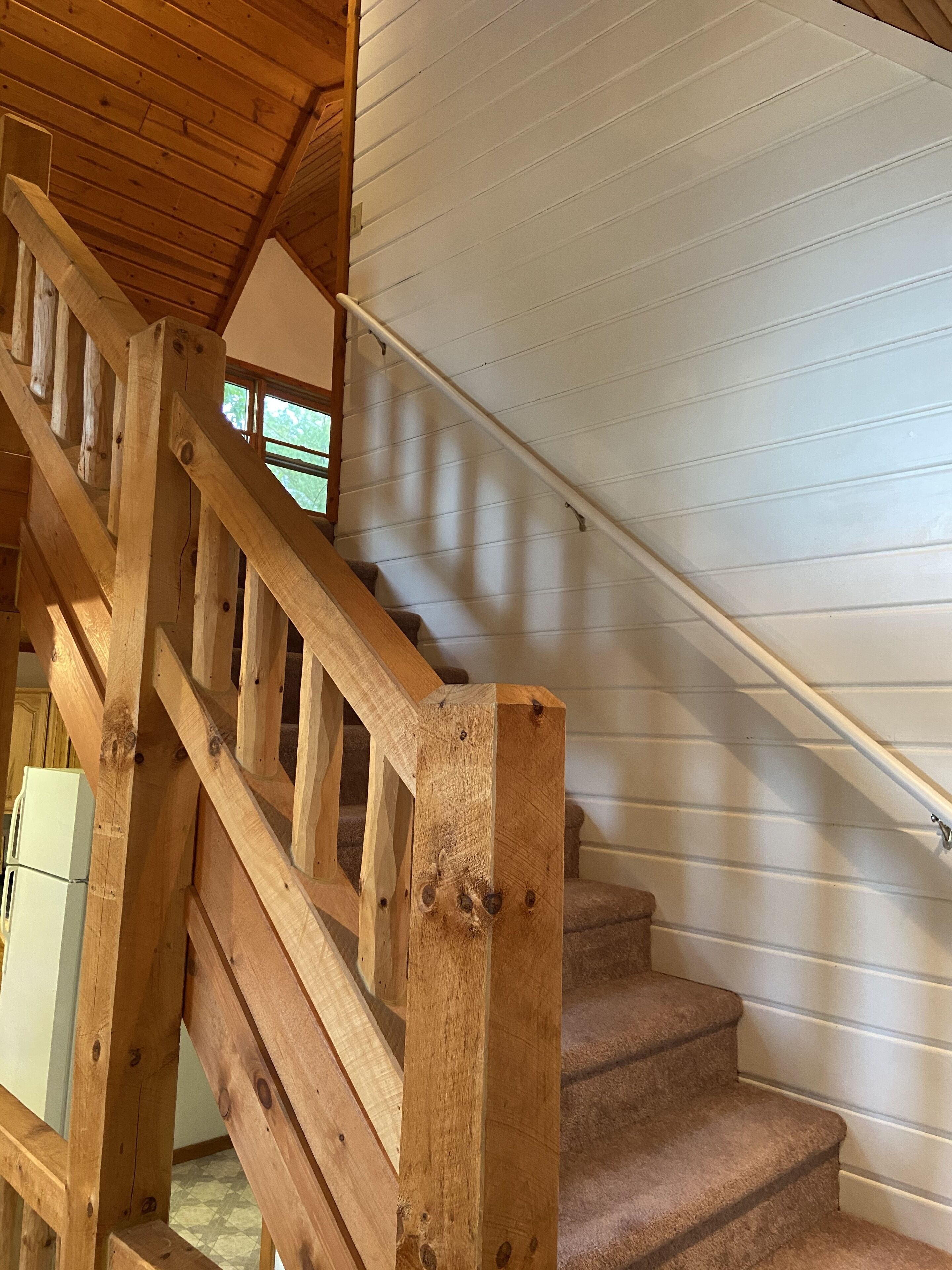 A wooden staircase with a handrail, leading to a landing with a white exterior wall.