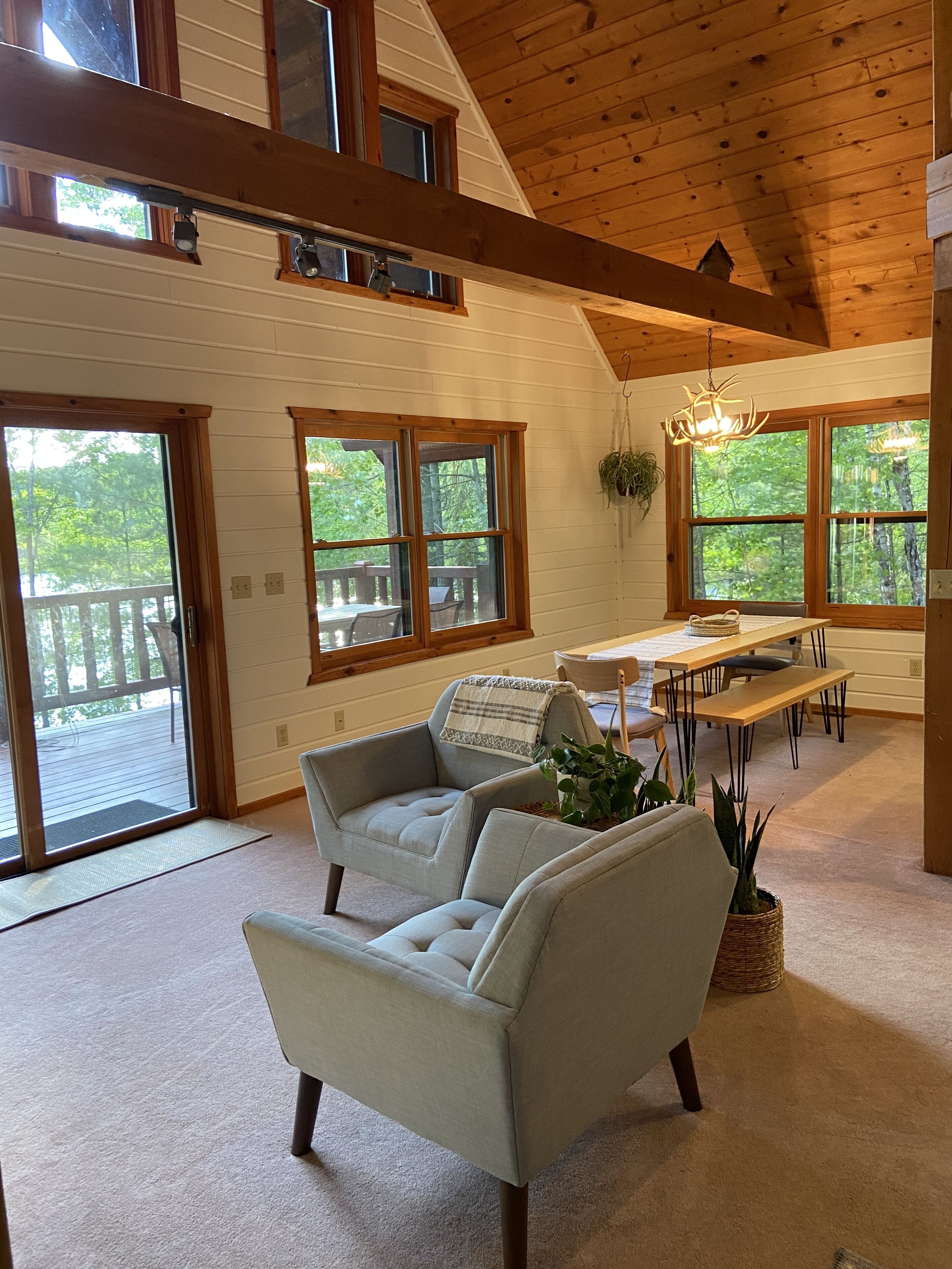 A spacious living area with a high ceiling, large windows, and a dining table.