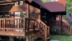 A log cabin with a wooden deck, stone foundation, and an American flag. - Søsterhus, Three Lakes/Eagle River Lake House (Eagle River)