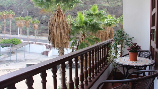 Ein Balkon mit Holzgeländer, einem runden Tisch mit Stühlen und Topfpflanzen.