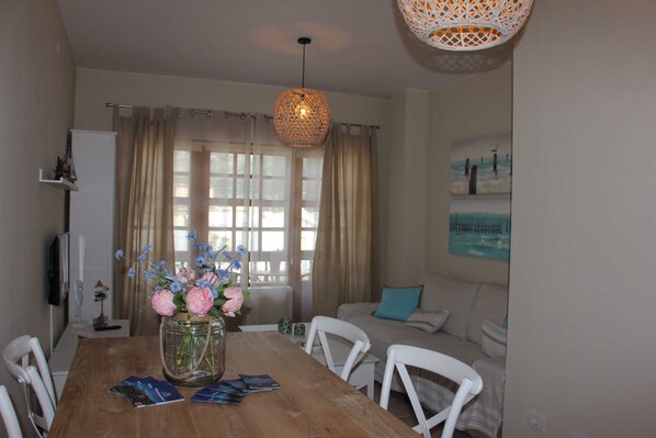 A dining area with a wooden table, white chairs, a vase with flowers, and a hanging light fixture.